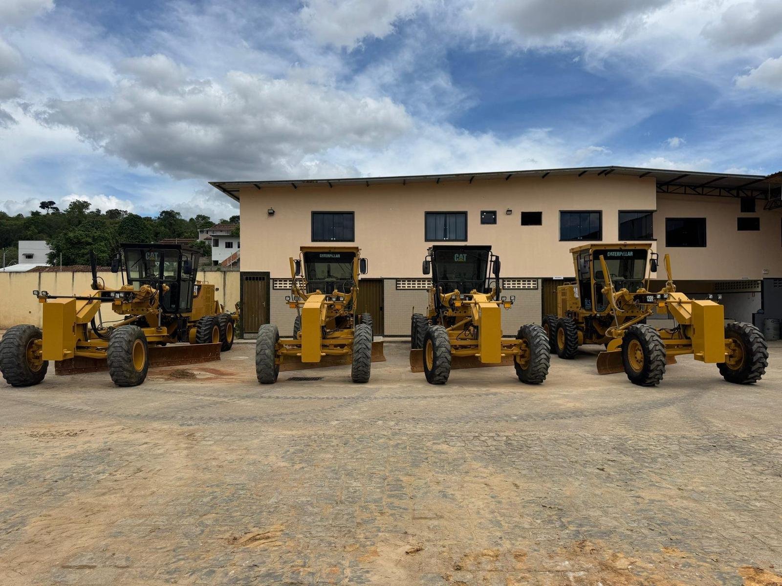 Quatro motoniveladoras Caterpillar alinhadas no pátio da sede da Escave