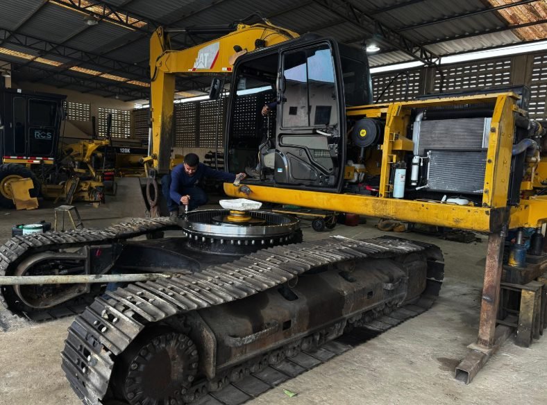 Mecânico da Escave trabalhando no rolamento de giro de uma escavadeira Caterpillar com a cabine removida, dentro da oficina